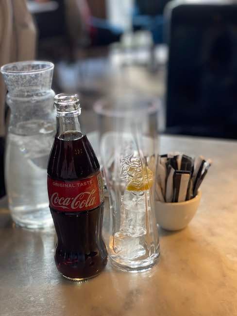 Photo of a classic bottle of Coca Cola next to a glass with ice and a slice of lemon