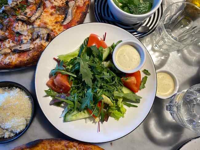 a photo of a side salad from Pizza Express with the dressing in a small bowl on the side of the plate.