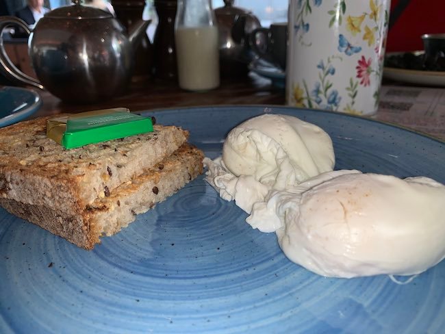 A photo of a plate of Poached Eggs and toast. There are two poached eggs on the right hand side and the toast is on the left hand side There is a pat of butter on top of the toast.