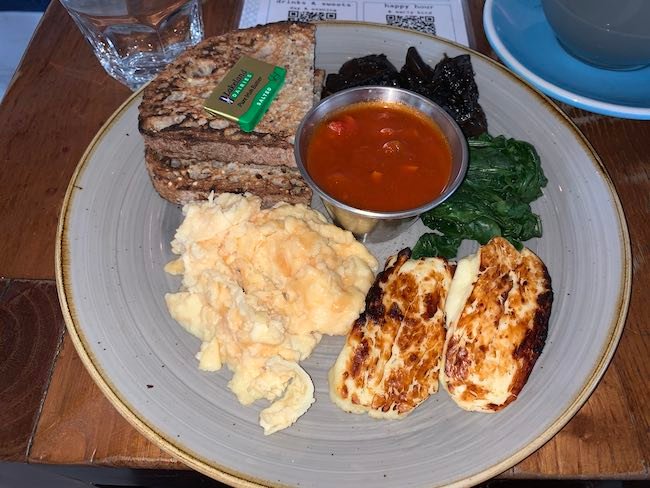 A photo of the veggie breakfast from Megans. There is toast, scrambled eggs, halloumi, spinach and grilled mushrooms.