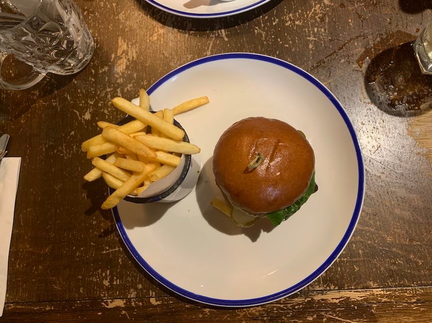 an over-head photo of a burger on a plate with a cup of french fries to the left