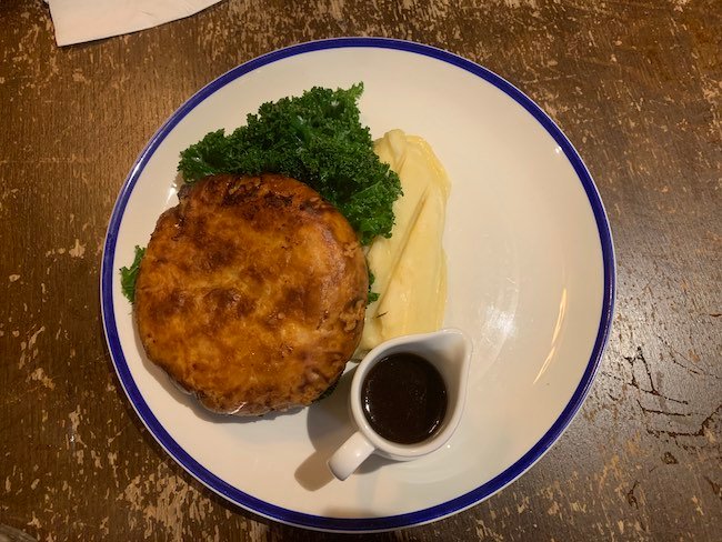 An overhead photo of the chicken pie from The Abbeville Clapham. One the plate is a jug of gravy, some kale and mashed potato