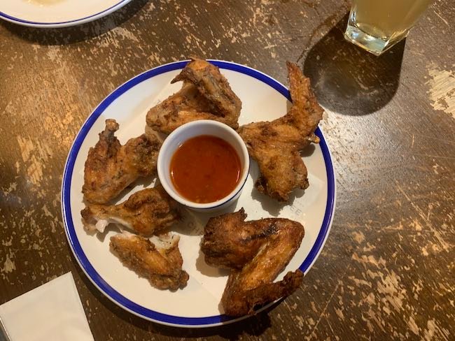 An overhead photo of a portion of Chicken Wings from The Abbeville Clapham. One of the chicken wings has been torn in half and in the centre of the plate is a bowl of lime and chilli dipping sauce