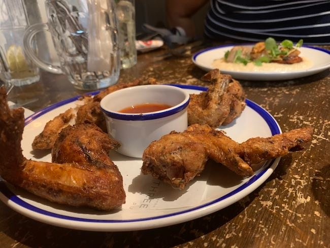 a low angled photo of a portion of Chicken wings from The Abbeville Clapham with a plate of scallops in the background